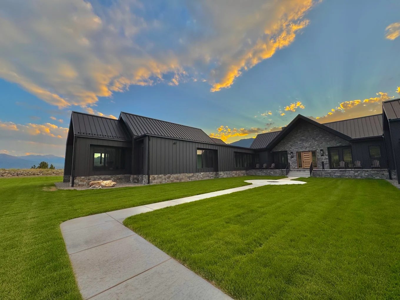 Modern mountain home at sunset with a manicured lawn and mountain views
